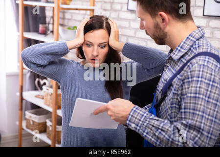 Shocked Woman Looking At Invoice Shown By Male Technician Stock Photo