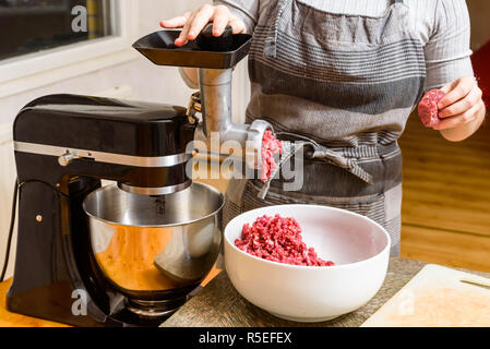 Person using domestic meat grinder while mincing meat at home. Stock Photo