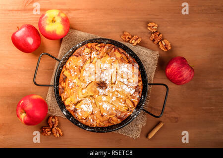 An apple pie, shot from above on a dark rustic wooden background with fresh apples, nuts, cinnamon, anise, and a place for text Stock Photo