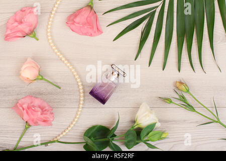Bottle of perfume, beads on a string, white and pink flowers, green leaves on wooden background. Woomen cosmetics. Top view. Stock Photo