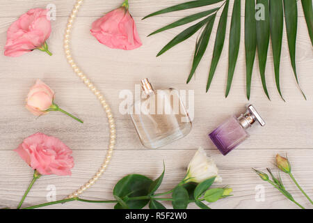 Two bottles of perfume, beads on a string, white and pink flowers, green leaves on wooden background. Woomen cosmetics. Top view. Stock Photo