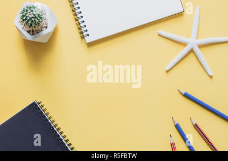 Office workplace minimal concept. Blank notebook with starfishes, cactus and pencils on yellow background. Stock Photo
