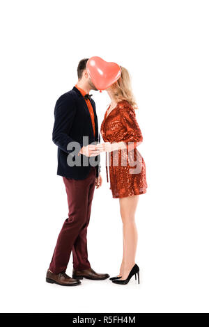 Attractive couple holding hands and kissing while hiding faces behind red balloon isolated on white Stock Photo