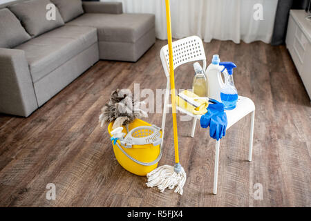 Bucket with dust wiper, sponges, chemicals bottles and mopping stick on the floor in the apartment. Cleaning service concept Stock Photo