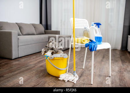 Bucket with dust wiper, sponges, chemicals bottles and mopping stick on the floor in the apartment. Cleaning service concept Stock Photo