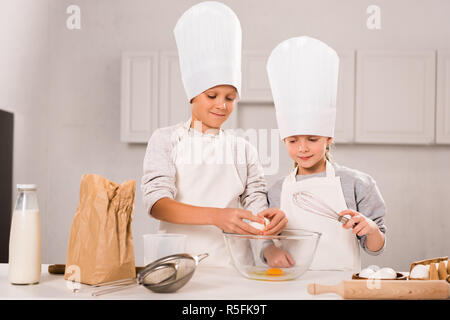 sister and brother breaking eggs into bowl during food preparation at table in kitchen Stock Photo