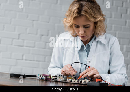 female electronic engineer with tester examining computer motherboard Stock Photo