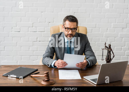 serious male judge working with papers and laptop in office Stock Photo