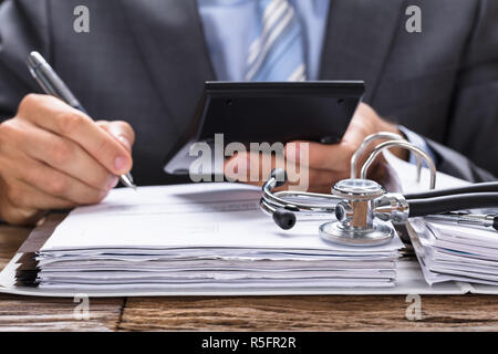 Businessman Calculating Invoice With Stethoscope On Documents Stock Photo
