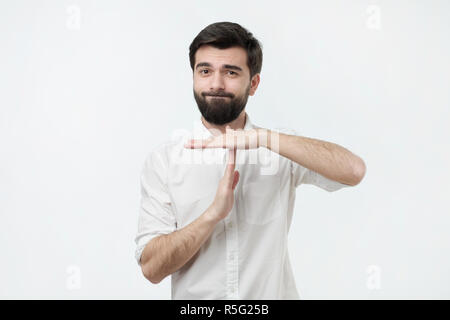 Spanish young man with black beard making time out gesture over grey background. I need a minute to rest. Stock Photo