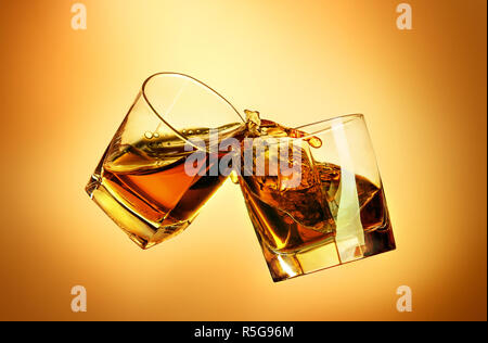 Two whiskey glasses clinking together on brown Stock Photo