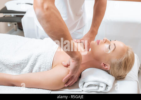 Male masseur doing shoulder massage to woman in spa salon Stock Photo