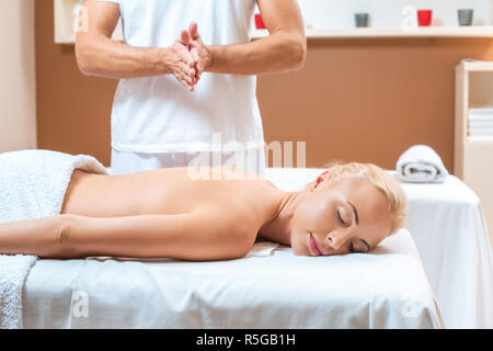Male therapist warming hands near blonde woman in beauty salon