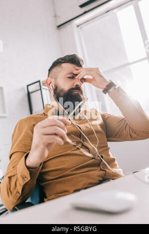 frustrated adult businessman in earphones with glasses in hand at workplace Stock Photo