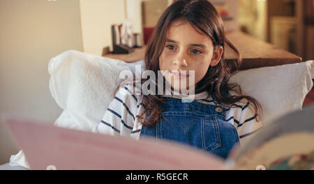 Young girl sitting at home reading a book.  Cute caucasian girl student engrossed in reading story book indoors. Stock Photo