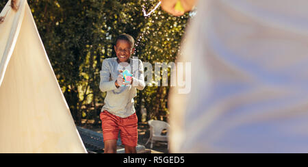 Little african boy playing squirt gun fight with friend in backyard. Kids enjoying playing water gun fight outdoors. Stock Photo