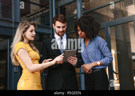 Group of businessman and women with digital tablet discussing work. Corporate professionals discussing work using digital tablet. Stock Photo