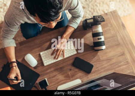 Overhead view of photographer editing photos at his studio. Photographer editing photos after a photo shoot using graphic tablet and stylus pen. Focus Stock Photo