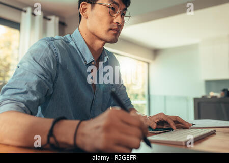 Male interior designer or architect working at his desk using graphics tablet and stylus pen for drawing. Interior designer in glasses sitting at a ta Stock Photo