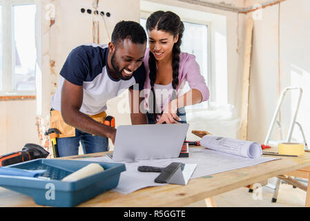 young african american woman pointing at laptop screen to boyfriend during renovation of home Stock Photo