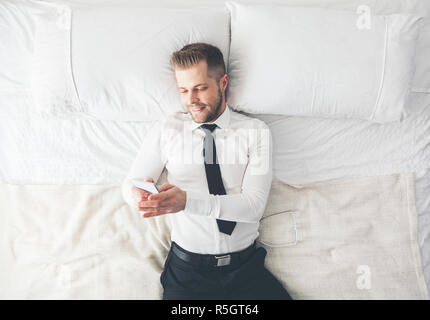 Top view. Handsome businessman lying on bed texting from his smartphone Stock Photo