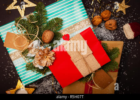 Colorful and decorated Christmas gifts on black background with snow, nuts and golden Christmas stars Stock Photo