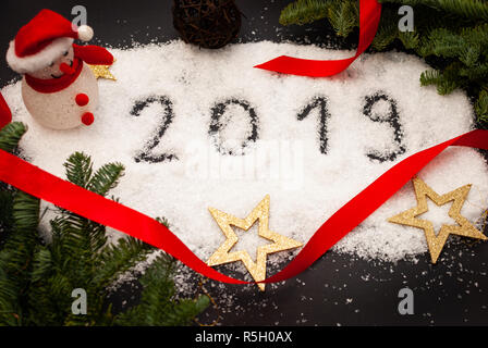 2019 written in snow on black background decorated with green branches and golden stars Stock Photo