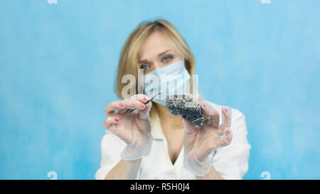 A woman lab worker examines the stones with tweezers takes the fibers of harmful asbestos. Stock Photo