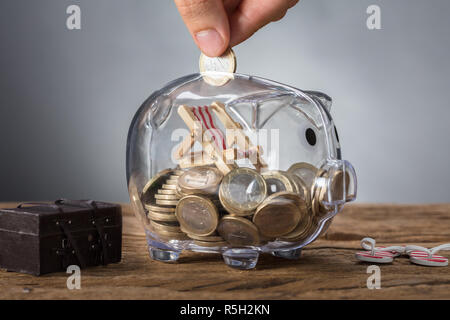 Hand Putting Coin In Transparent Piggy Bank With Deck Chair Stock Photo