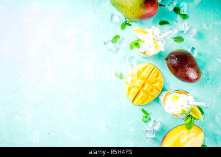 Tropical sweet dessert drink. mango milkshake or smoothie cocktail, with mango slices, mint and ice cubes, light blue background copy space Stock Photo
