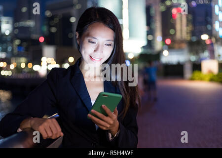 Businesswoman working on cellphone in the city at night Stock Photo