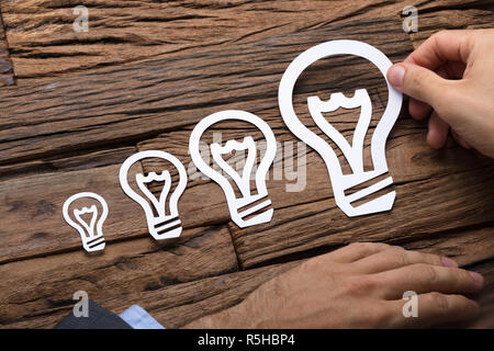 Businessman Arranging Paper Light Bulbs In Increasing Order Stock Photo