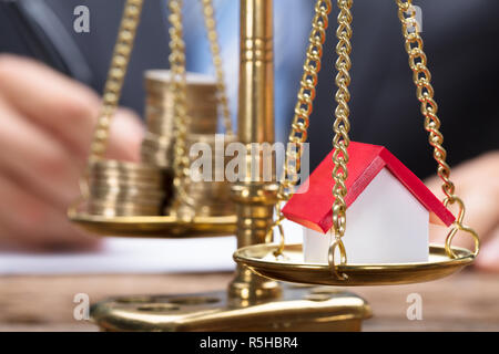 Businessman With Model Home And Coins On Golden Weighing Scale Stock Photo