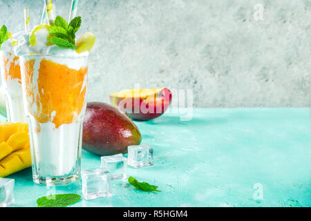Tropical sweet dessert drink. mango milkshake or smoothie cocktail, with mango slices, mint and ice cubes, light blue background copy space Stock Photo