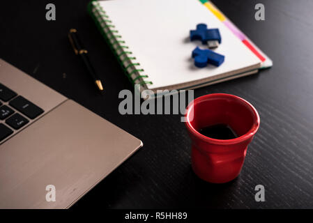 still life with blocknote, labtop, pen and a red cup of coffee over a black office desk. symbol of job Stock Photo