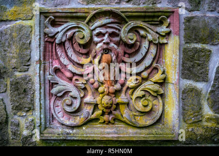 Old and colourful waterspout made of stone looking like a face Stock Photo