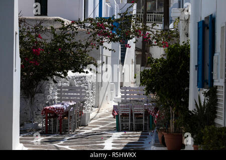 Narrow alley with chairs and tables on a suunny day in Mykonos Town, Greece Stock Photo