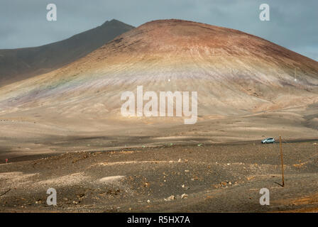 A view from a road en-route to Playa Blanca, Lanzarote, with a dramatic volcano swathed in multi coloured lava and pumice deposits. Stock Photo