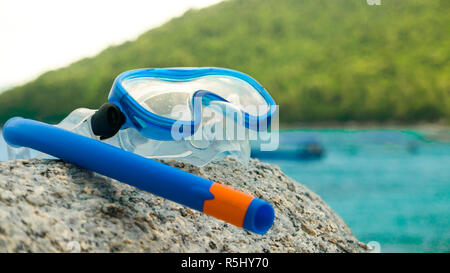 Snorkeling equipment: snorkel and diving google on the stone. Tropical island, sea, beach and boats in background. Stock Photo