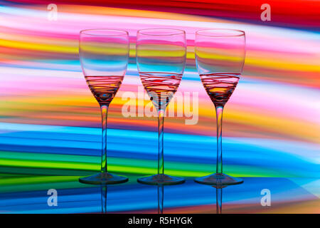 Three wine glass / glasses  with colourful light painting behind them