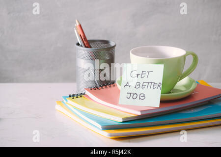 Green cup, notebooks and sticker with text - get a better job on light background. Toned business concept with copy space Stock Photo