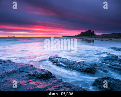 A firey sunrise over Bamburgh castle and the Harkness Rocks. Stock Photo