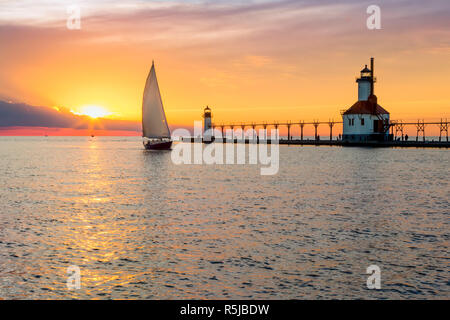 A sailboat rounds the breakwater near sunset on the longest day of the year by the Lighthouses at St. Joseph, Michigan with people fishing from and wa Stock Photo