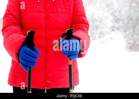 Human in red sport jacket and blue gloves holds two Sticks for hiking in winter season on snow background close up Stock Photo