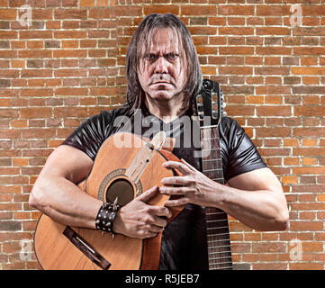 The rocker with a broken guitar on background of the brick wall. Guitarist on acoustic guitar. Stock Photo