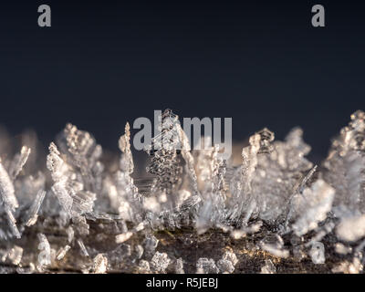 Frost crystals forming beautiful  geometrical shapes on wood surface against black background Stock Photo