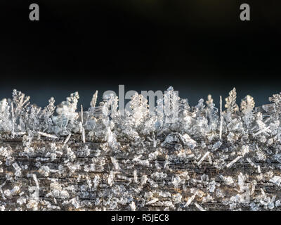 Frost crystals forming beautiful  geometrical shapes on wood surface against black background Stock Photo