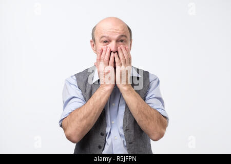 Mature, shocked, surprised man with hands covering mouth, eyes wide open in full disbelief Stock Photo