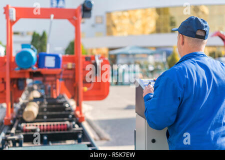 Worker pressing buttons on CNC machine control board in factory. Stock Photo