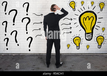 Confused Businessman Looking At Question Marks And Light Bulbs Stock Photo